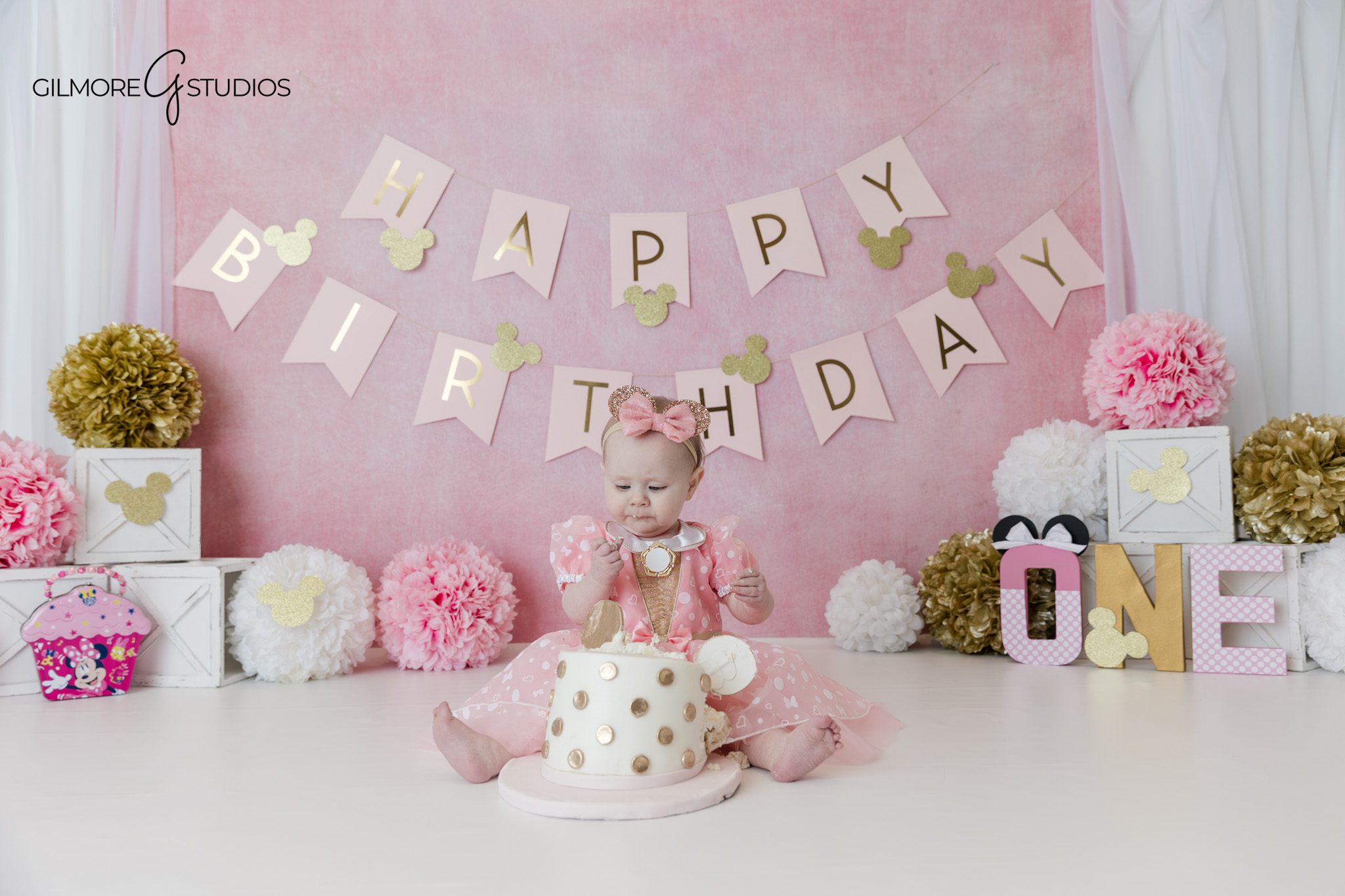 Baby girl in pink dress for themed first birthday portraits
Minnie Mouse inspired cake smash with pink flowers and gold accents